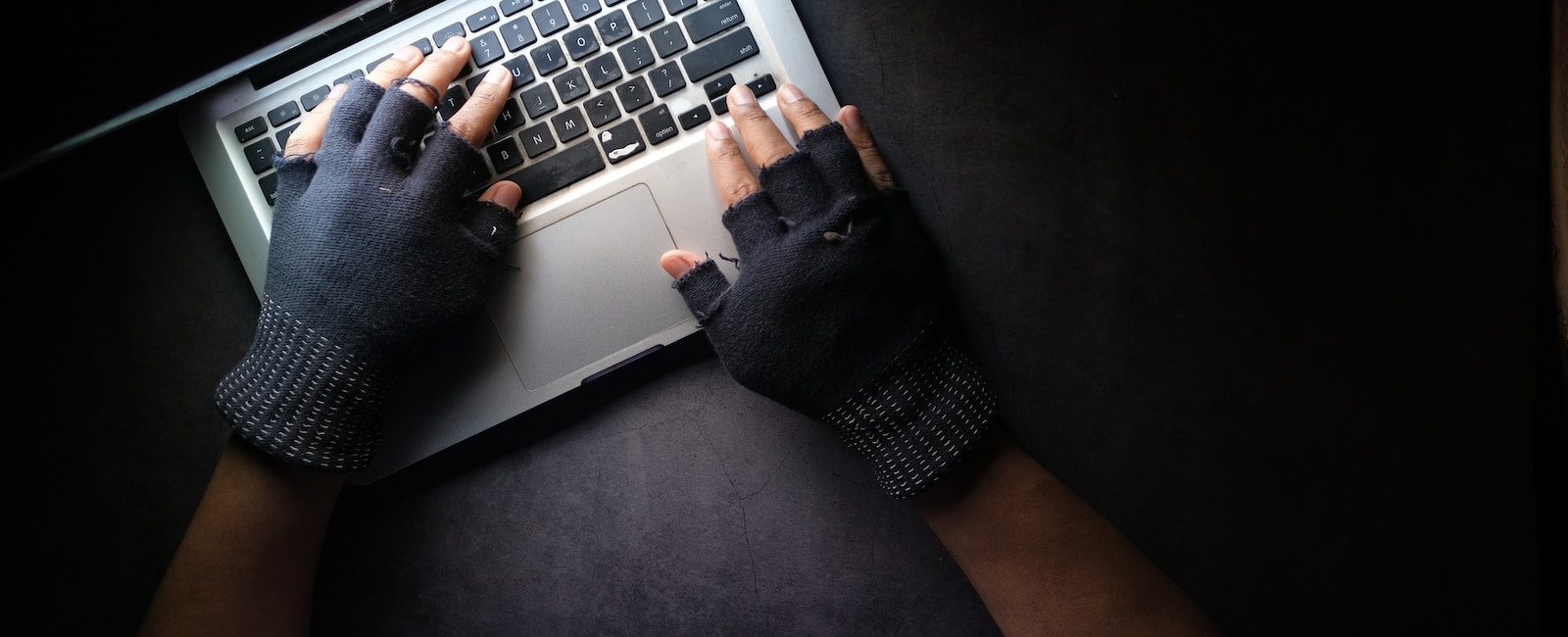 Person typing on laptop wearing fingerless gloves, focused on keyboard productivity in low-light setting