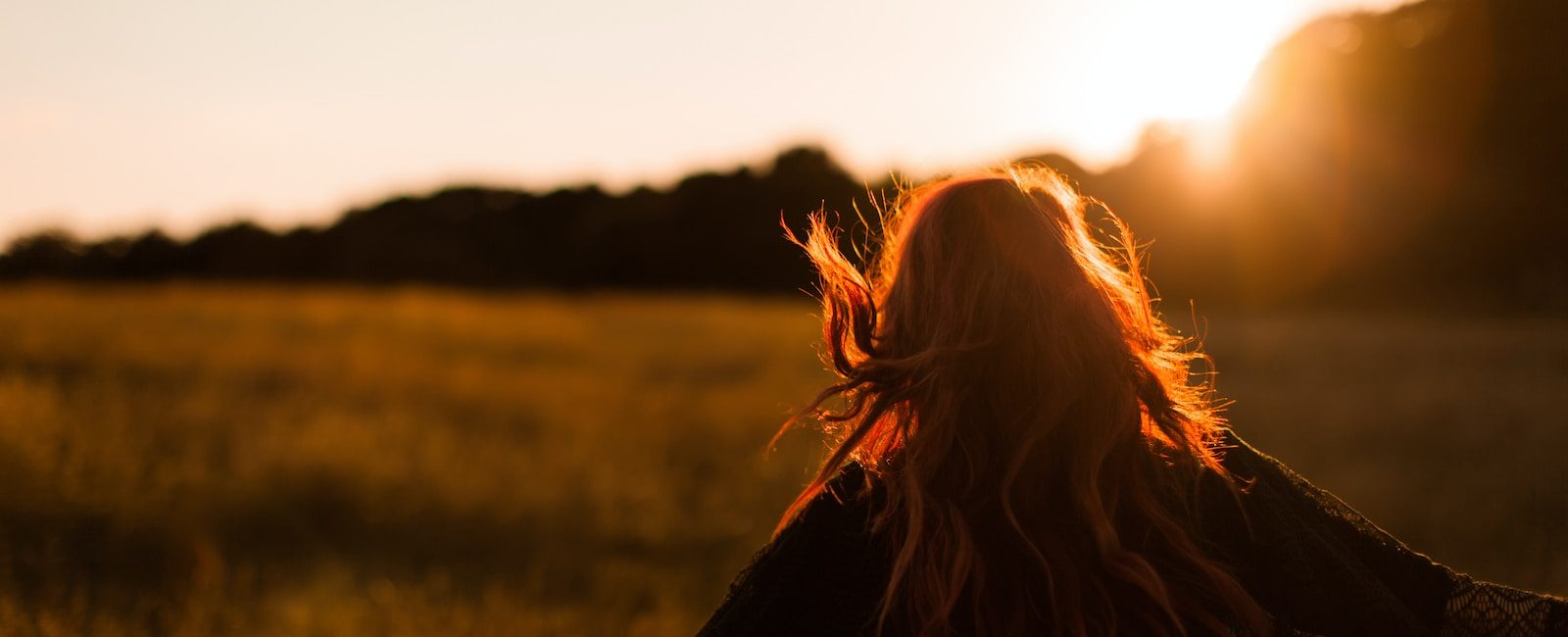 Woman with flowing hair enjoying a sunset in a meadow, surrounded by golden light and nature's tranquillity