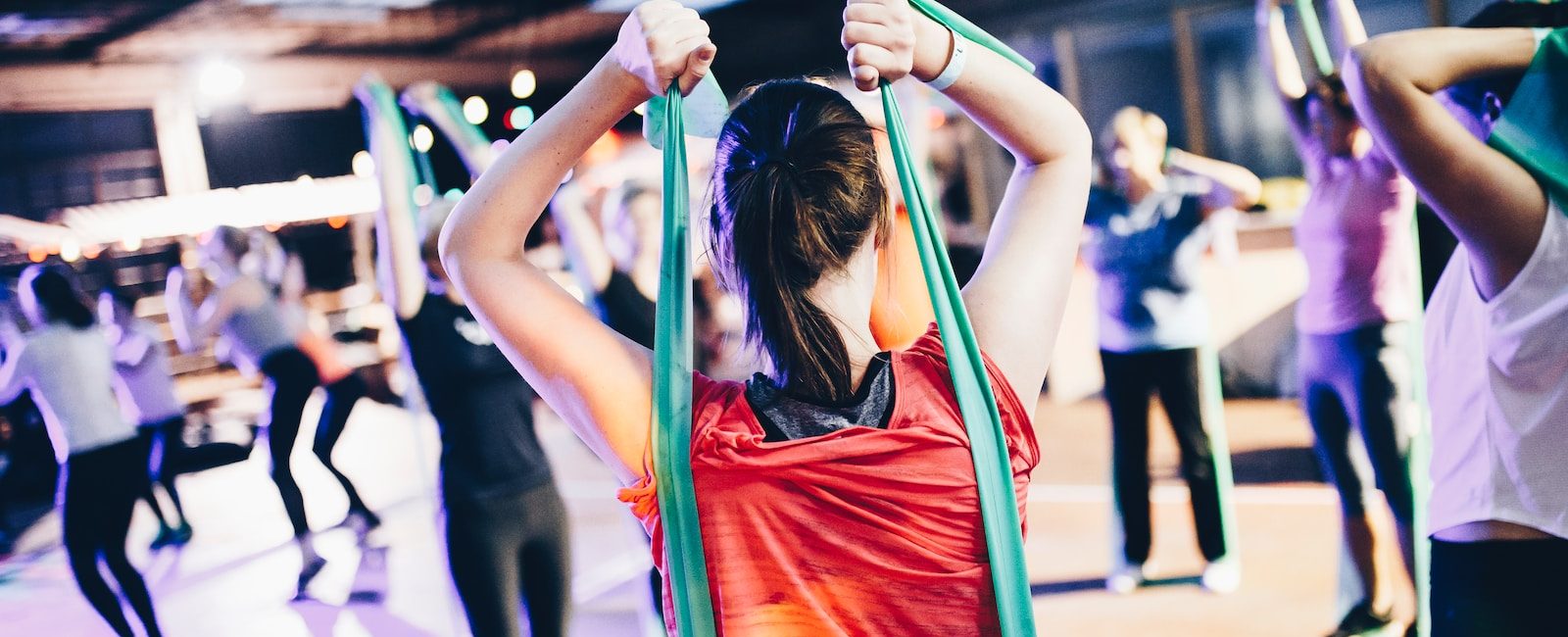 Group fitness class participants using resistance bands in a bright, spacious gym setting
