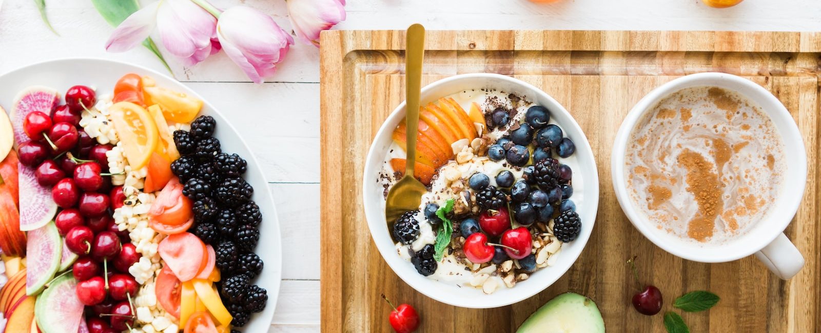 Healthy breakfast spread with colourful fruit salad, mixed berries bowl, avocado, coffee, and honey on a wooden board