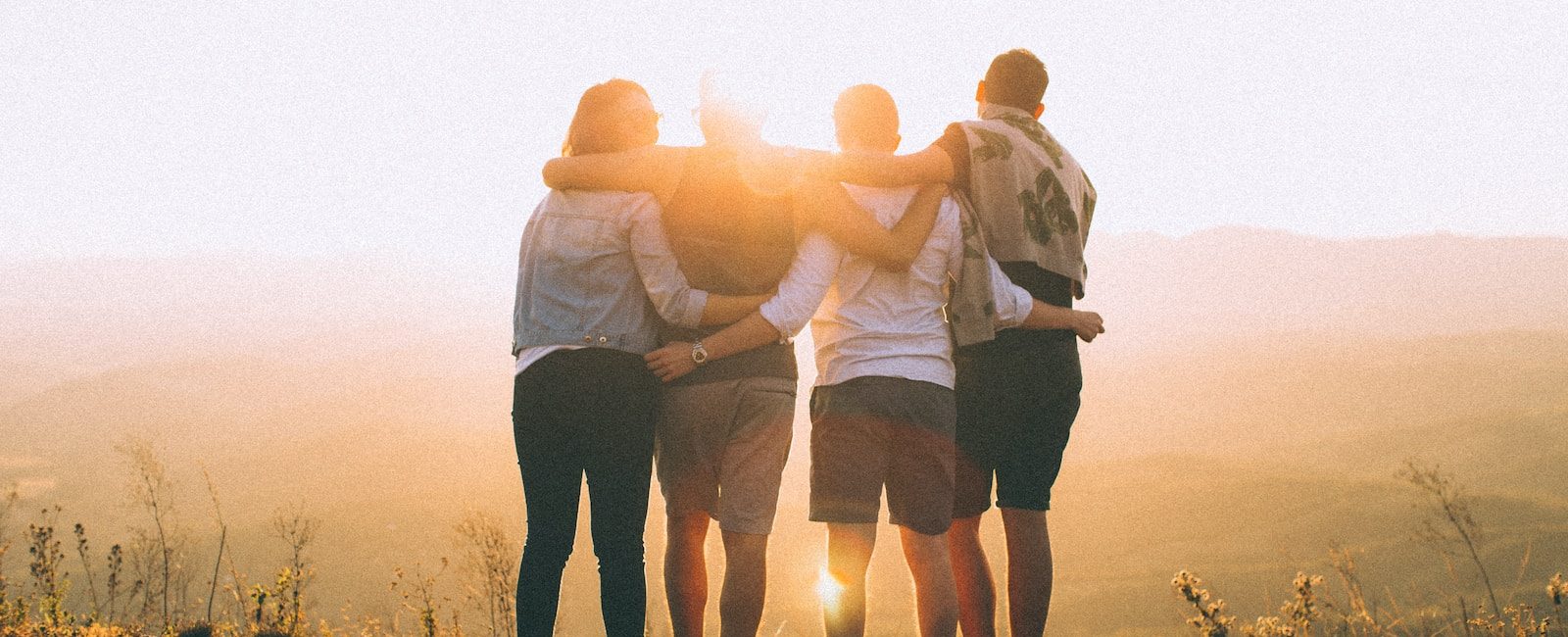 Friends embracing at sunset on a hilltop, enjoying the beautiful view and warm sunlight