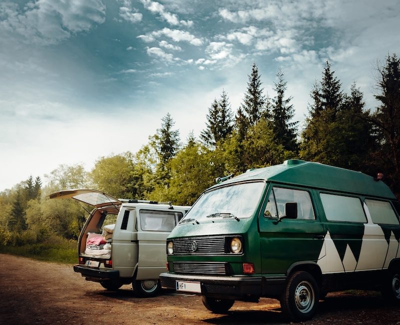 Vintage campervans parked in a scenic forest setting under a cloudy blue sky, perfect for a road trip adventure