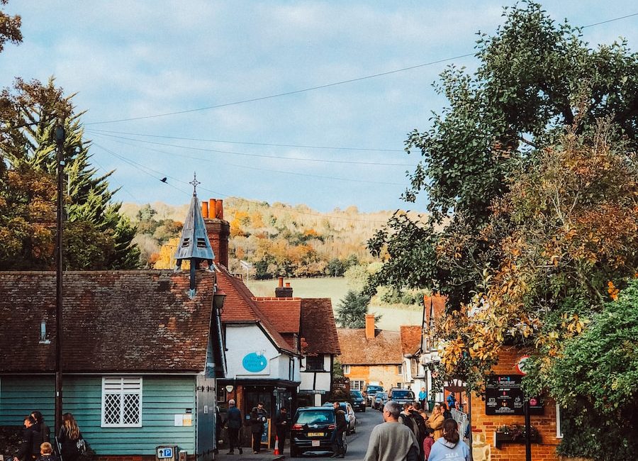 Charming village street in autumn with people walking, surrounded by quaint cottages and colourful foliage under a cloudy sky