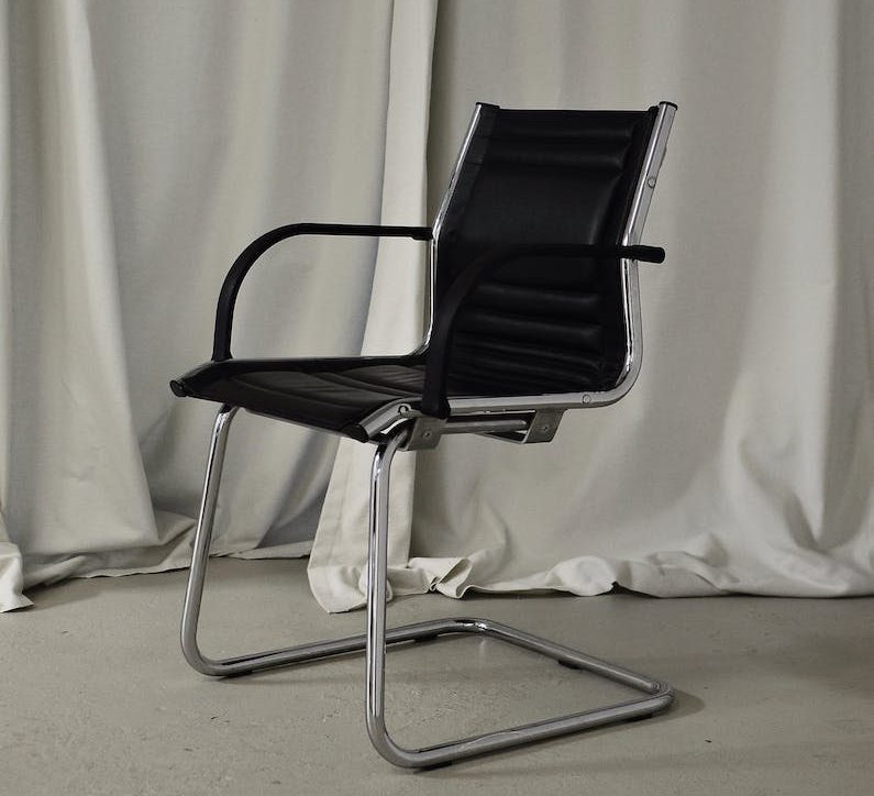 Black leather office chair with chrome frame in front of neutral curtains