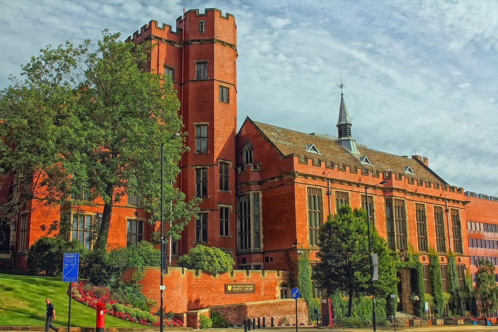 Historic red-brick university building with tower and green landscape in the foreground
