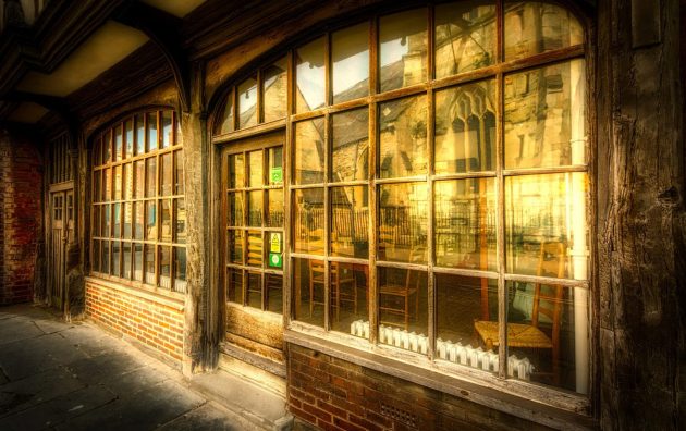 Vintage storefront with large wooden windows reflecting historic buildings on a sunny street in England