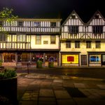 Night view of illuminated historic Tudor buildings on a quiet street, showcasing timber-framed architecture