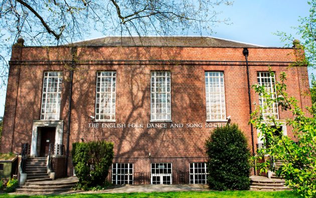 Red-brick building of the English Folk Dance and Song Society surrounded by greenery on a sunny day