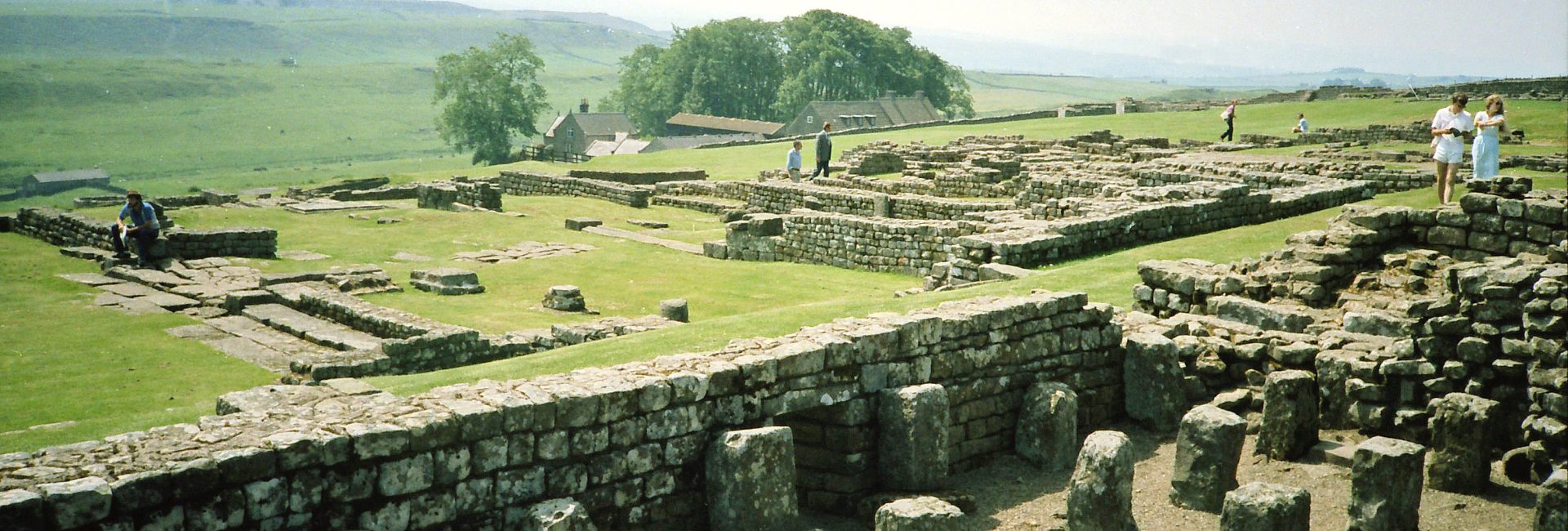 Ancient Roman ruins of Hadrian's Wall with green rolling hills and visitors exploring the historic site