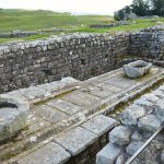 Ancient stone ruins with a view of lush green fields at Hadrian's Wall, showcasing Roman architecture and craftsmanship