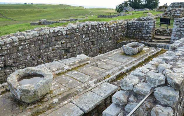 Ancient stone ruins with a view of lush green fields at Hadrian's Wall, showcasing Roman architecture and craftsmanship