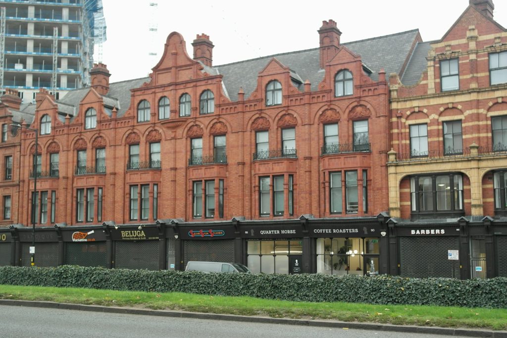 Historic red brick building with shops and cafes on street level in urban setting, featuring Victorian architectural details