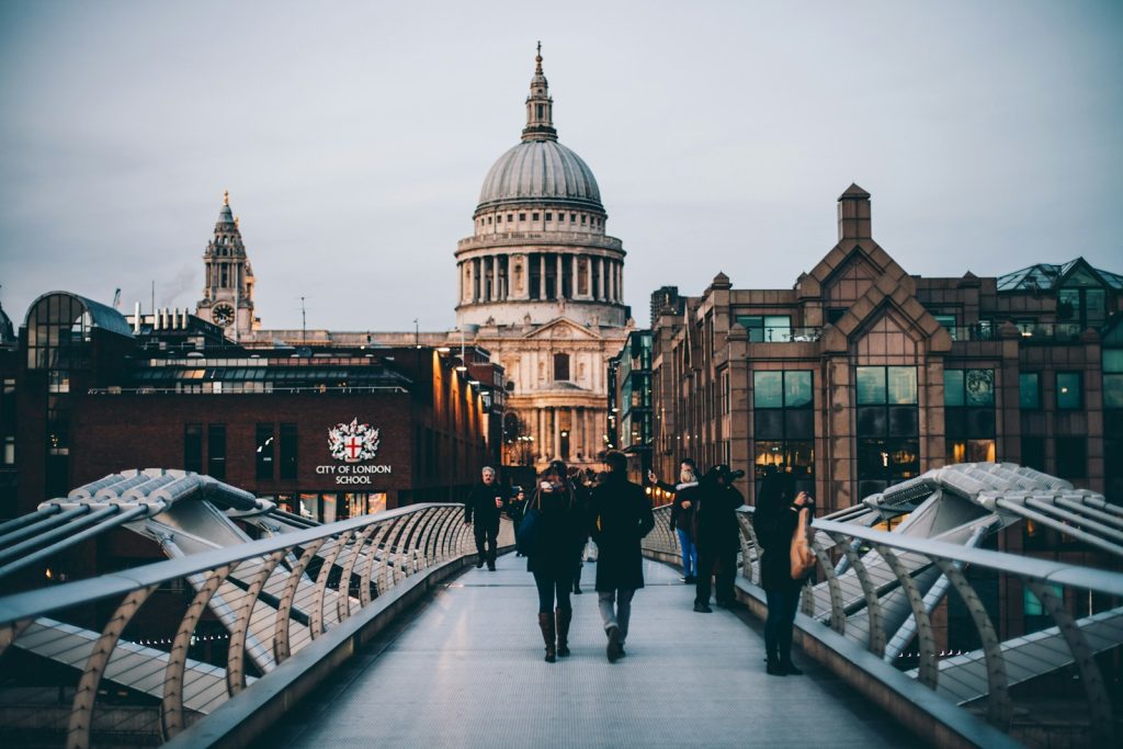 People walking on the Millennium Bridge towards St Paul's Cathedral, London at dusk, with city buildings in view