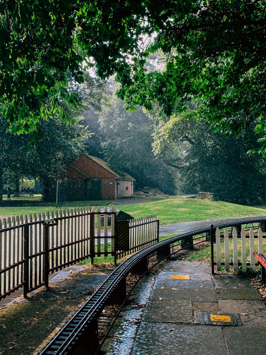 Rainy day in a park with a small railway track, surrounded by lush green trees and a rustic wooden shed