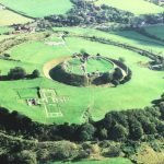 Aerial view of historic English earthwork and ruins amidst lush green landscape near village houses