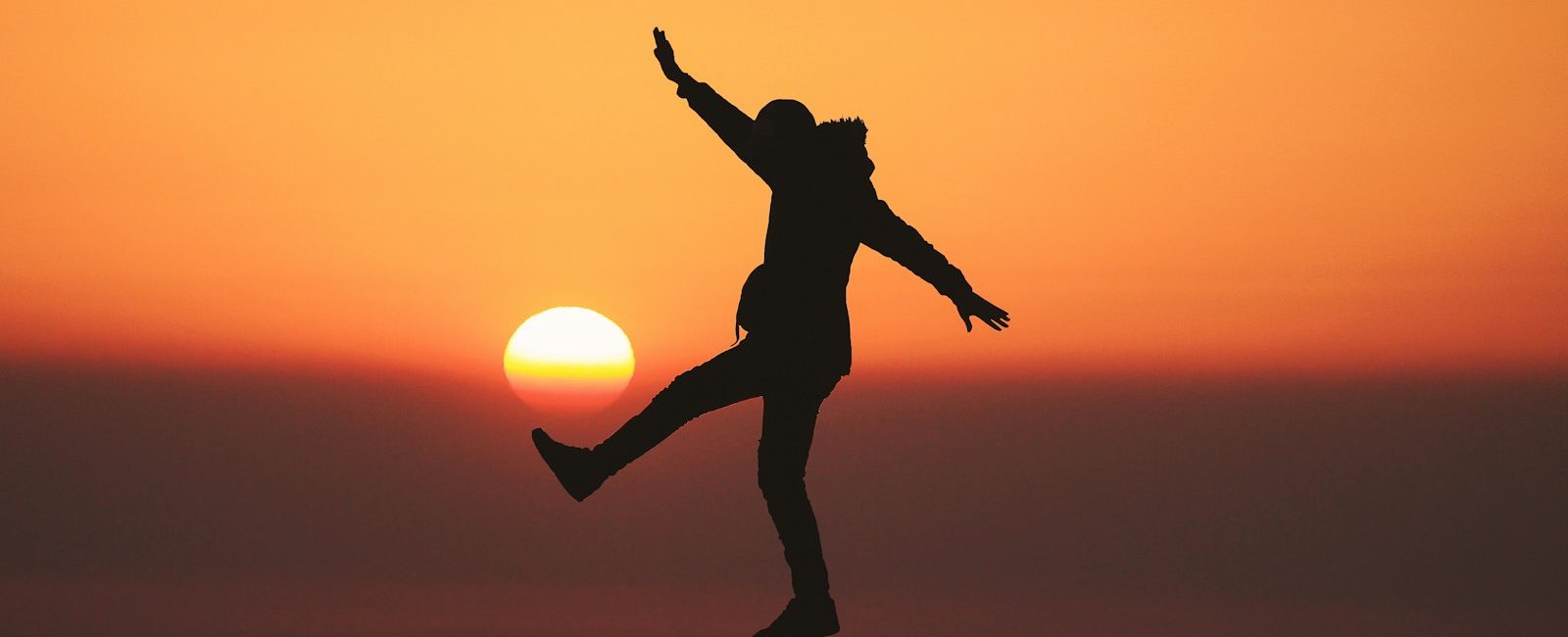 Silhouette of person balancing at sunset with orange sky and sun in background