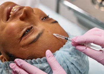 Person receiving a cosmetic injection on the forehead in a clinic setting, wearing protective cap and gloves