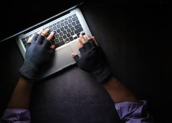 Person typing on laptop wearing fingerless gloves, focused on keyboard productivity in low-light setting
