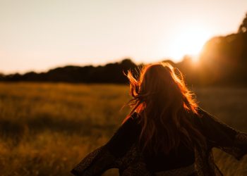 Woman with flowing hair enjoying a sunset in a meadow, surrounded by golden light and nature's tranquillity