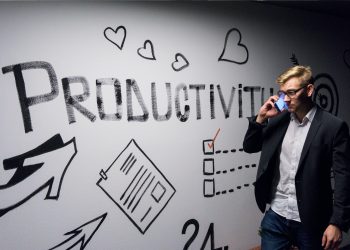 Man in a suit talking on phone in front of productivity-themed wall art featuring hearts, arrows, and checklists