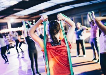 Group fitness class participants using resistance bands in a bright, spacious gym setting