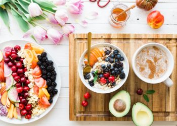 Healthy breakfast spread with colourful fruit salad, mixed berries bowl, avocado, coffee, and honey on a wooden board