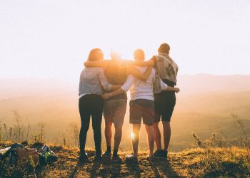 Friends embracing at sunset on a hilltop, enjoying the beautiful view and warm sunlight