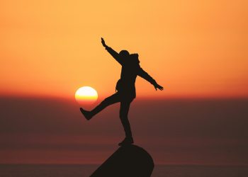 Silhouette of person balancing at sunset with orange sky and sun in background